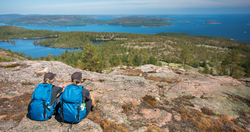 Två personer som sitter på en klippa och tittar ut över skog och hav..