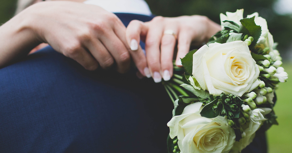 Närbild av en bruds händer som håller i en blombukett och sin brudgum.