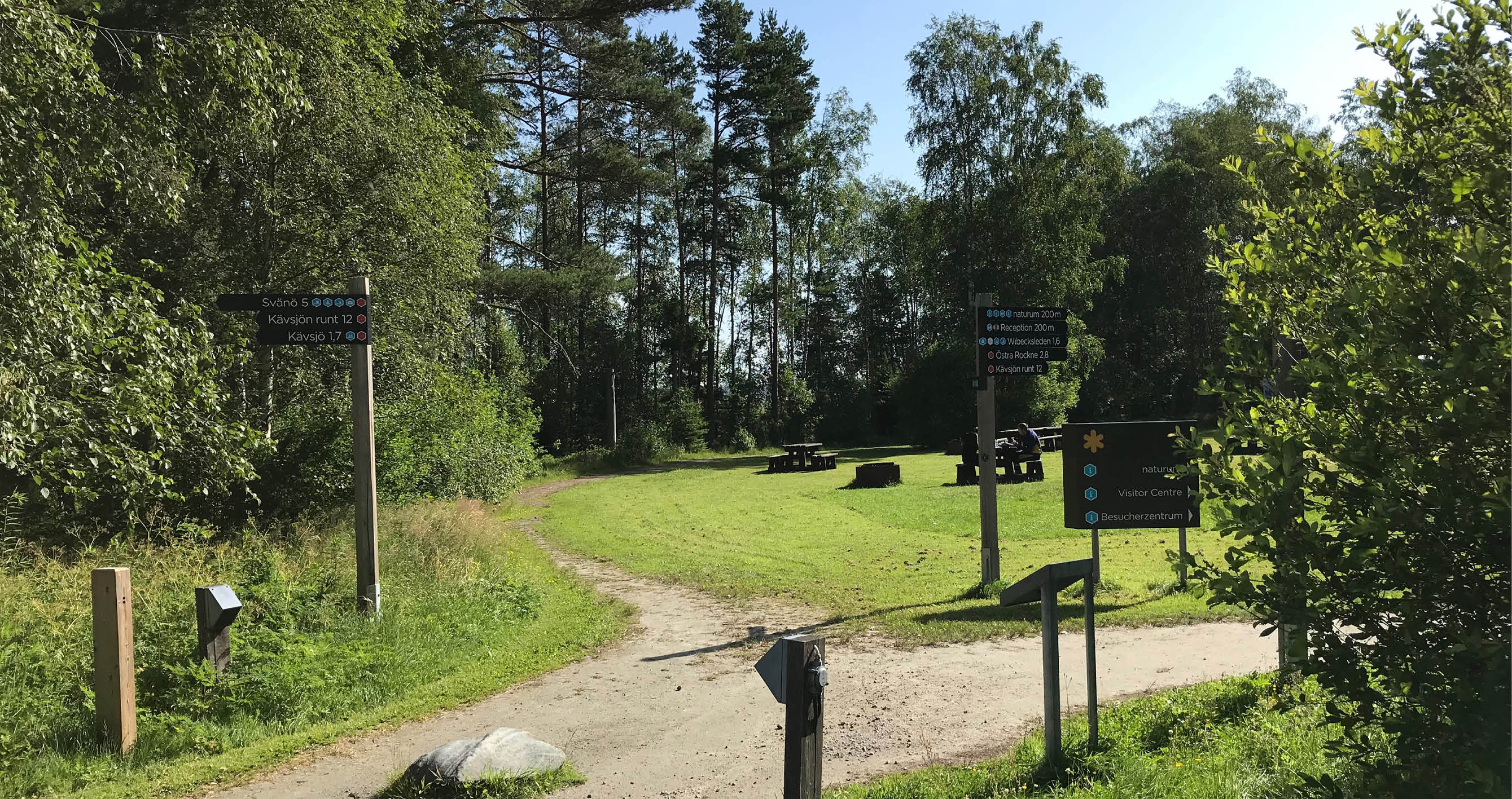 Huvudentré Store Mosse, vägriktningsskyltar på stolpe och bänkbord på öppen gräsmatta