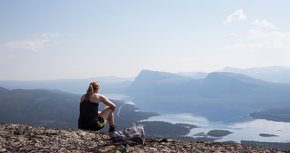 En kvinna sitter på en höjd och blickar ut över bergen.