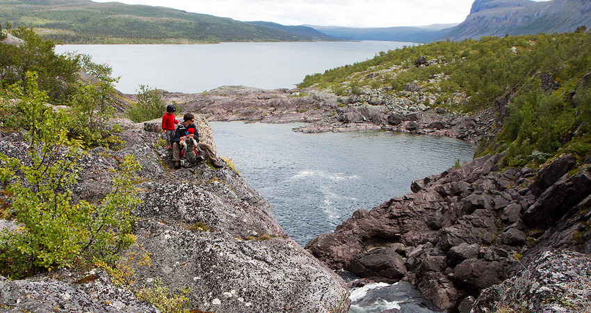 En familj står vid en klipphäll bredvid en sjö.