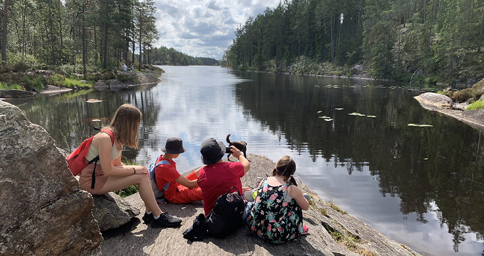 Människor sitter på en klipphäll vid strandkanten och blickar utåt sjön.