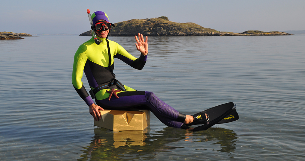 A man with a diving suit, cyclops, snorkel and fins is sitting on a golden crown out in the water.